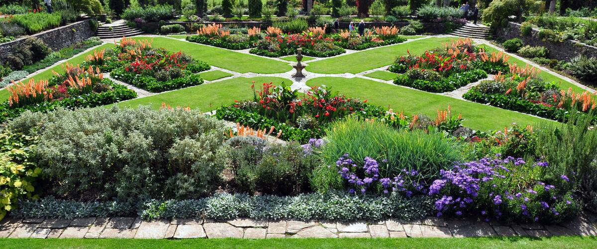 A formal garden with symmetrical flower beds, a central fountain, and a stone pathway.