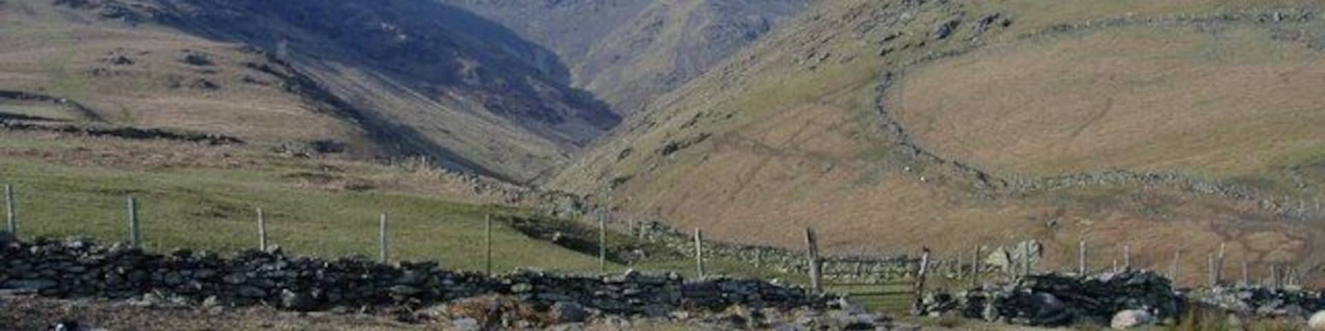 Paisagem montanhosa com ovelhas pastando e um muro de pedra.