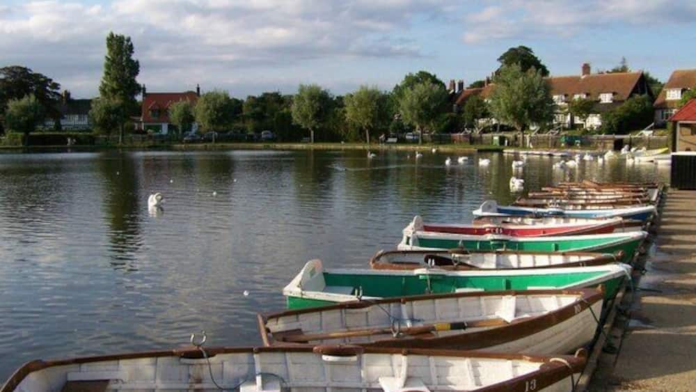 Ein ruhiger See mit mehreren kleinen Booten, die am Ufer vertäut liegen, umgeben von Bäumen und Häusern.