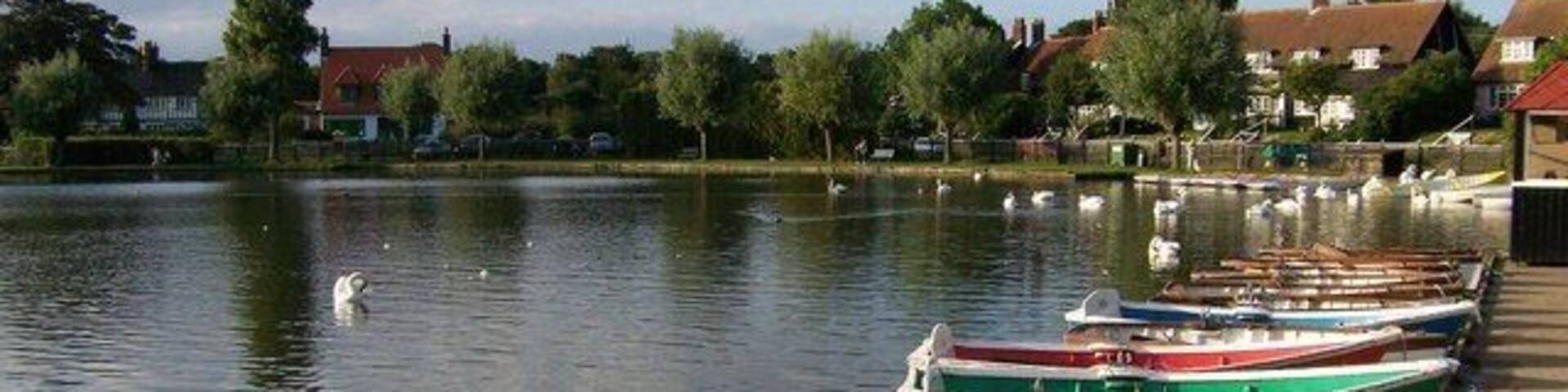 A calm lake with several small boats docked along the shore, surrounded by trees and houses.