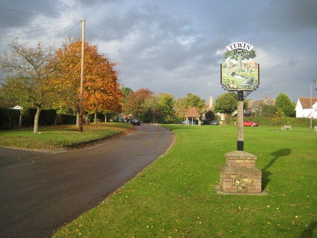 A rural road with a signpost in the center, surrounded by trees and houses.