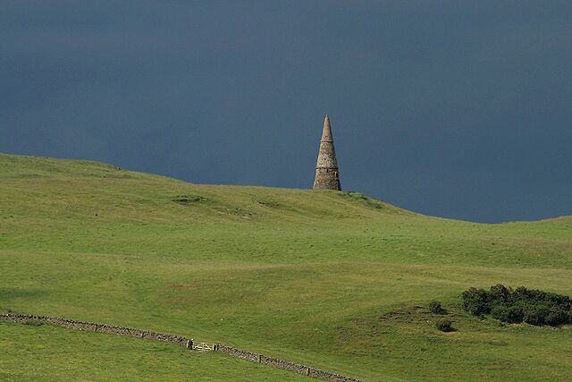 A grassy hill with a conical stone structure in the distance.