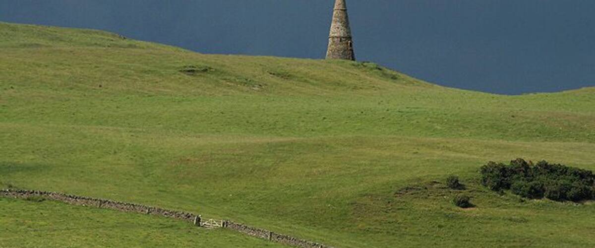 A grassy hill with a conical stone structure in the distance.