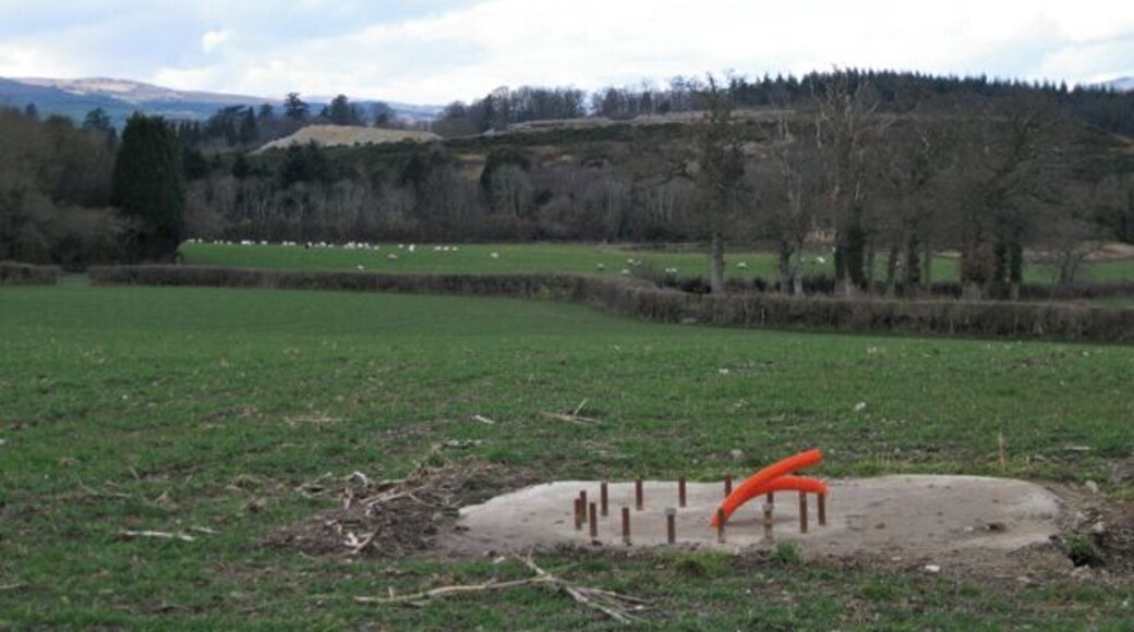 Work in progress by Greycoat Lane Looks like a water point for livestock. Beyond the sheep is a high mound of old clay waste from the Stover Quarry, clothed with gorse and grass. A pile of fresh, light-coloured clay waste appears beyond it, with woodlands and exotic conifers around Stover School showing beyond that.