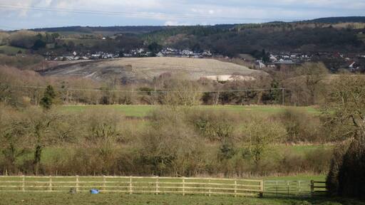 River Teign floodplain above Teign Bridge. Seen from the Teigngrace lane below Mount Pleasant. The river is over 500m away beyond old and new field boundaries and the line of the Stover Canal/disused railway/Templer Way. Out of sight beyond the river is an old claypit on the Broadway site behind which passing sunshine lights a hill of clay waste in the course of construction in SX8673 (as far as I can judge). The shaping is more sensitive than that of the older mounds at Newbridge and Preston but it is an intrusion nonetheless, overbearing in the vicinities of New Cross (right of centre) and 'Key Transport Pond'.