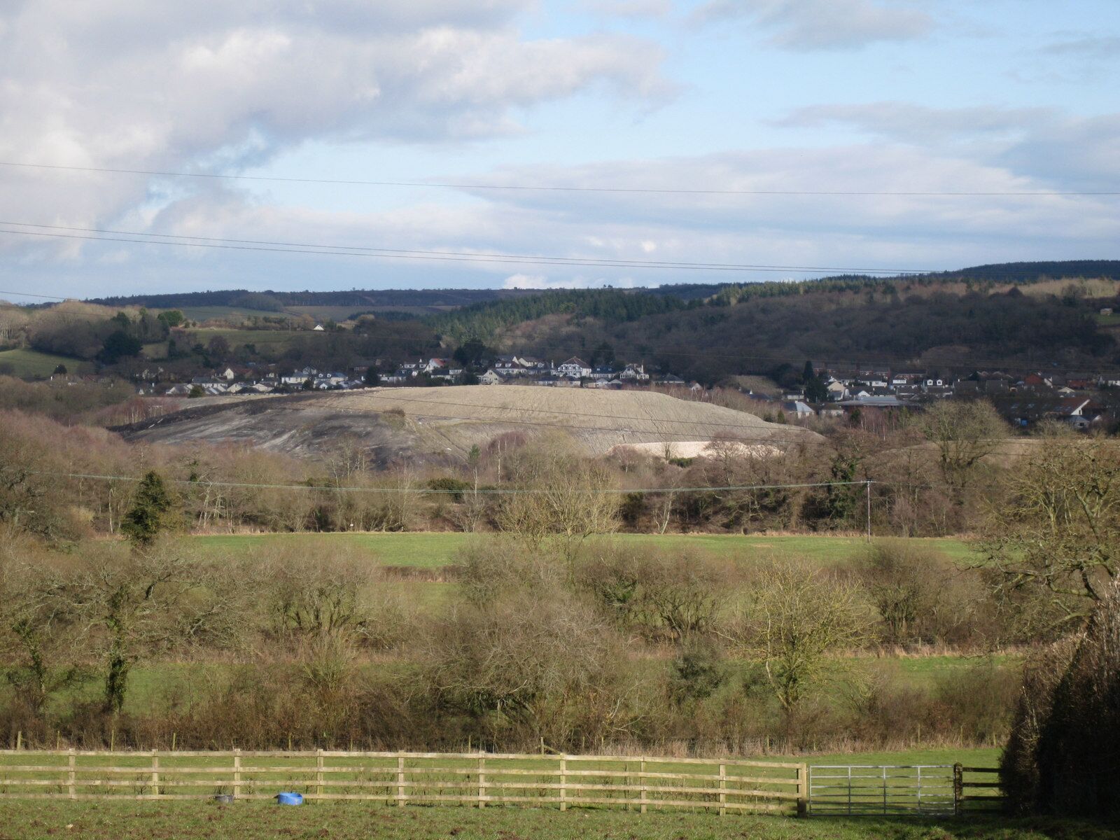 A rural landscape with a village, rolling hills, and a clear sky.