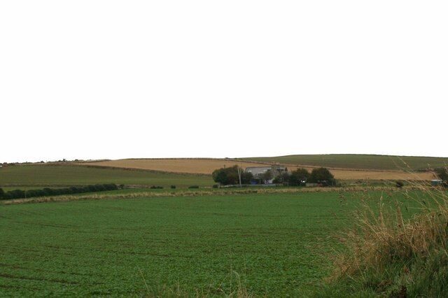 A green field with a building in the distance and rolling hills.