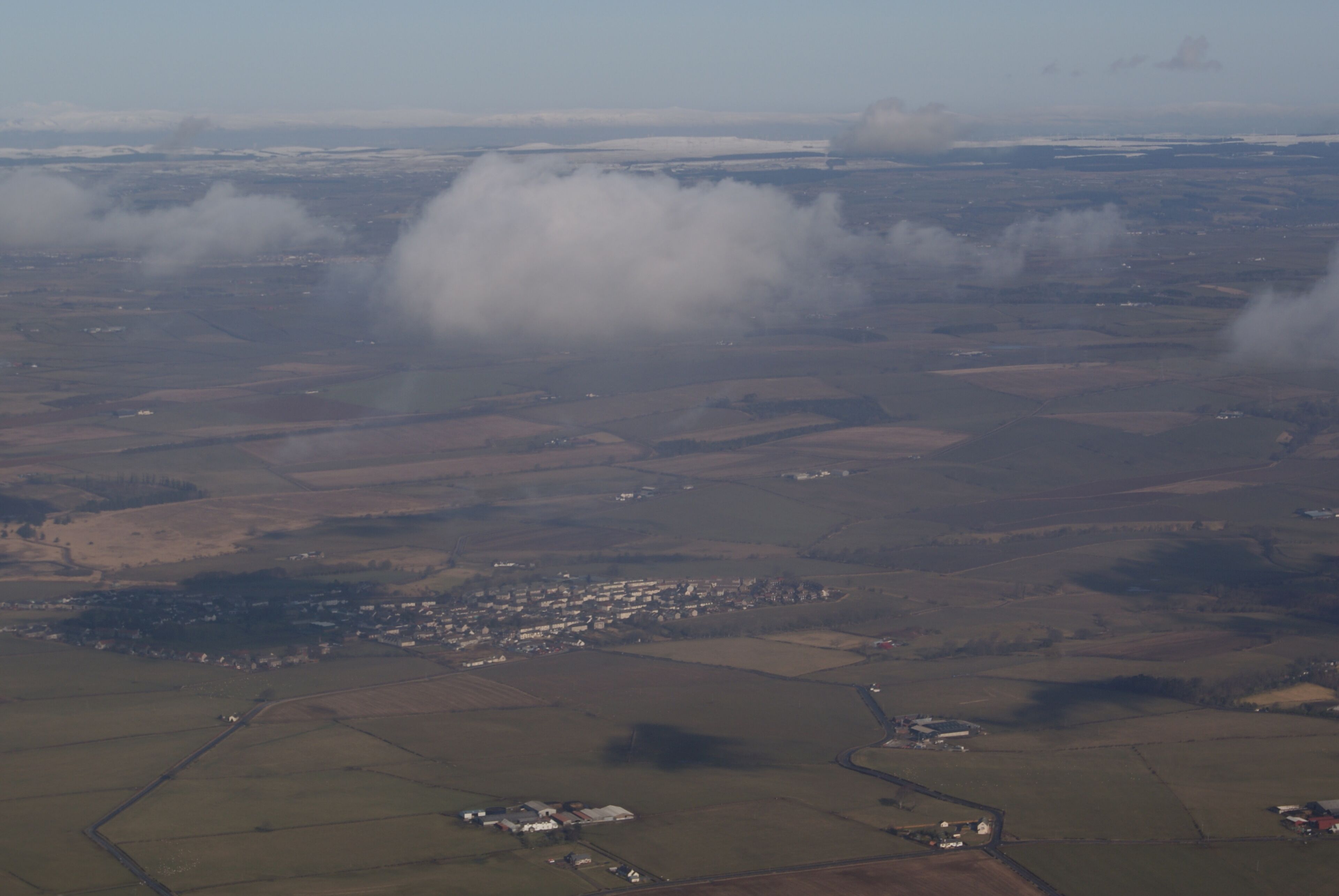 An aerial view of a rural landscape with fields, a small town, and a large cloud formation.
