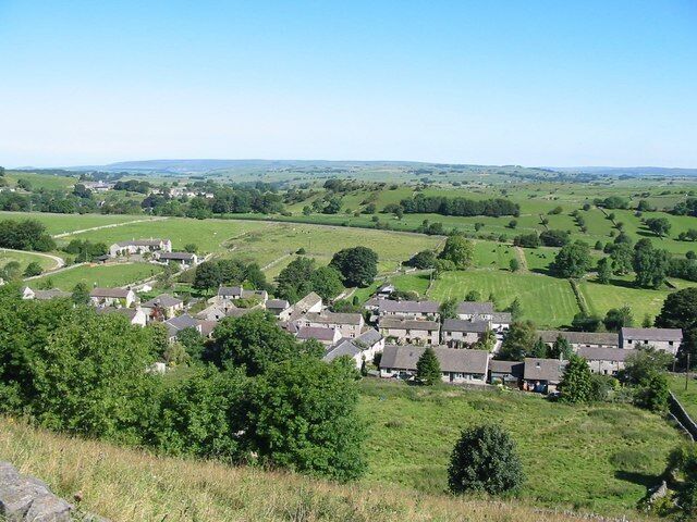 Un pueblo rural con casas en una ladera, rodeado de campos verdes y árboles.