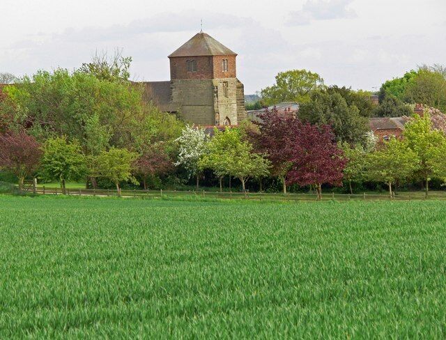 A church with a tower, surrounded by a green field and trees with autumn foliage.