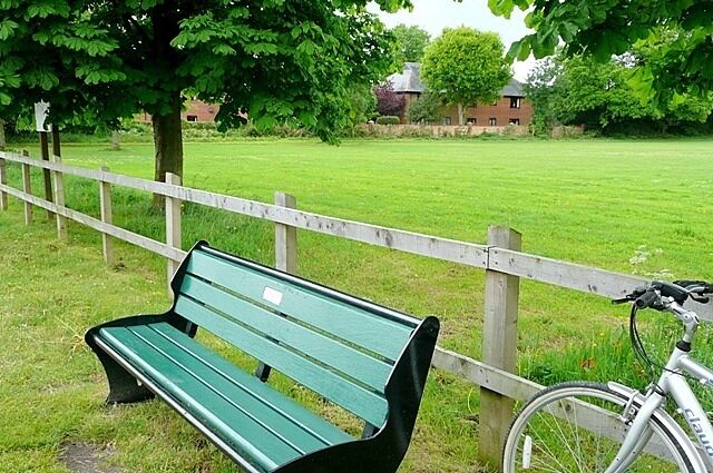 A green park bench, a white bicycle, and a wooden fence.