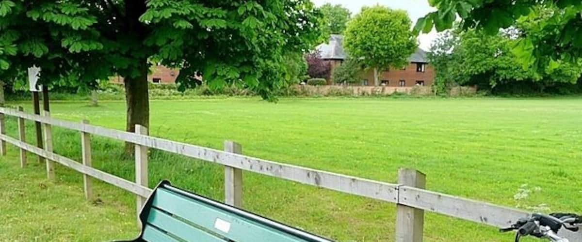 A green park bench, a white bicycle, and a wooden fence.