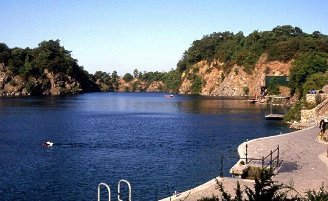 A calm river with a boat, a rocky hillside, and a paved walkway.