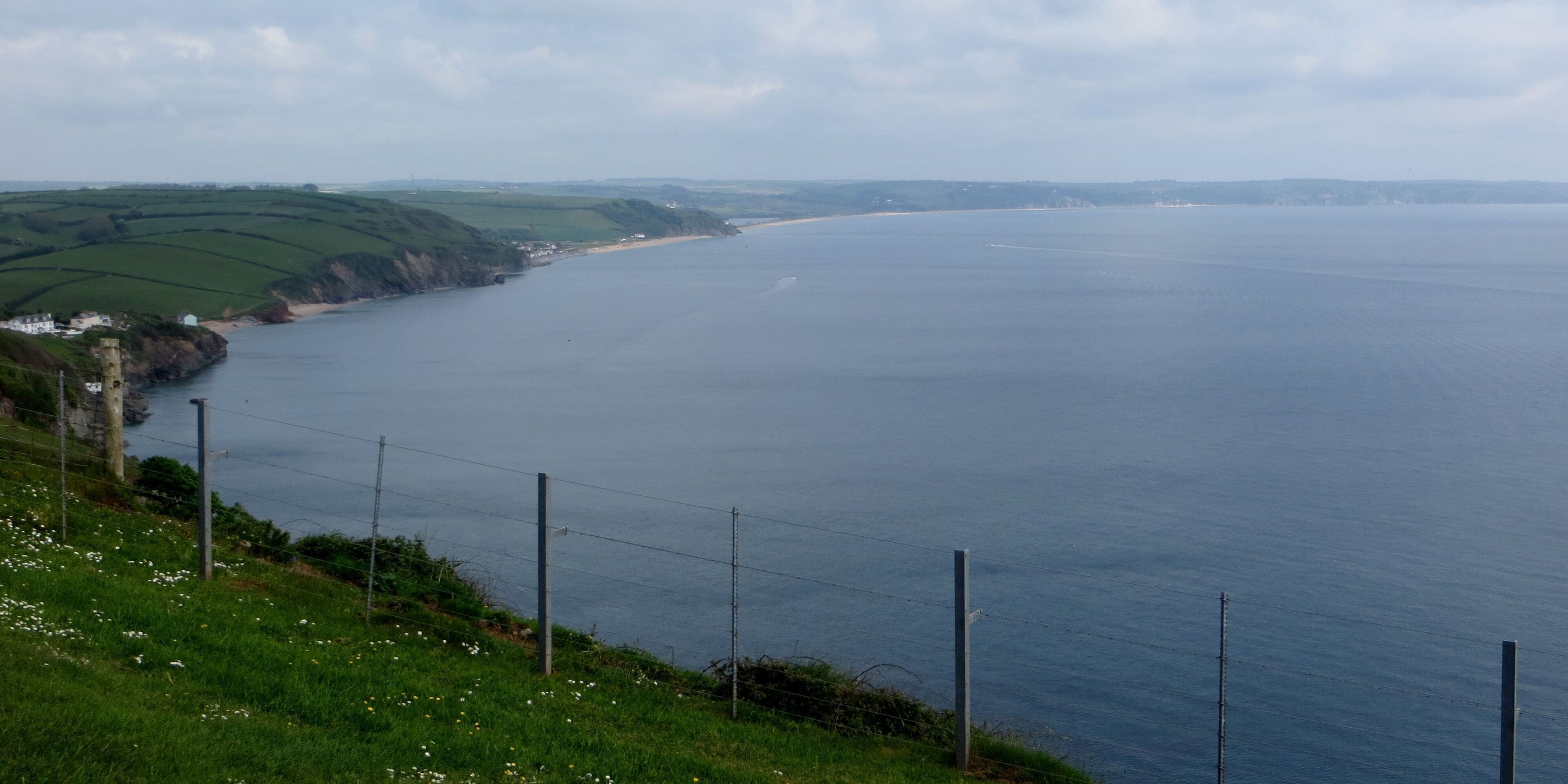 A coastal landscape with a grassy hill, a beach, and a body of water.