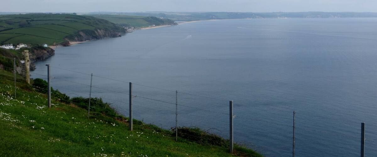 A coastal landscape with a grassy hill, a beach, and a body of water.