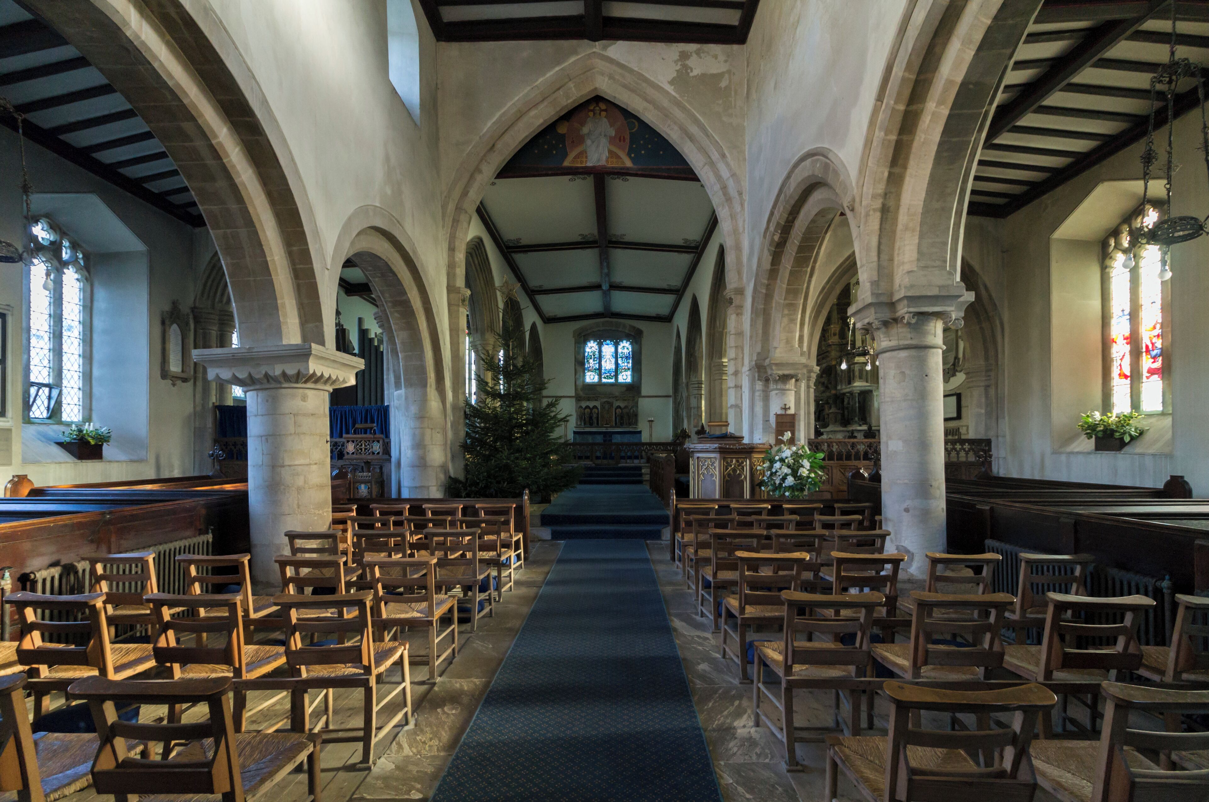 A church interior with wooden pews, a central aisle, stained glass windows, and a vaulted ceiling.