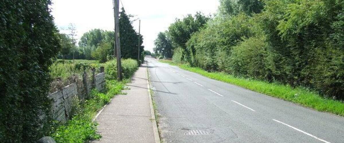 A rural road with a sidewalk, greenery, and a stone marker.