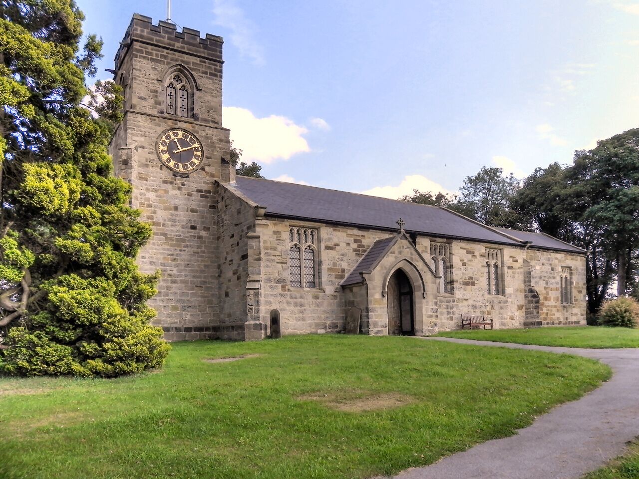 A stone church with a clock tower and a large tree in front.