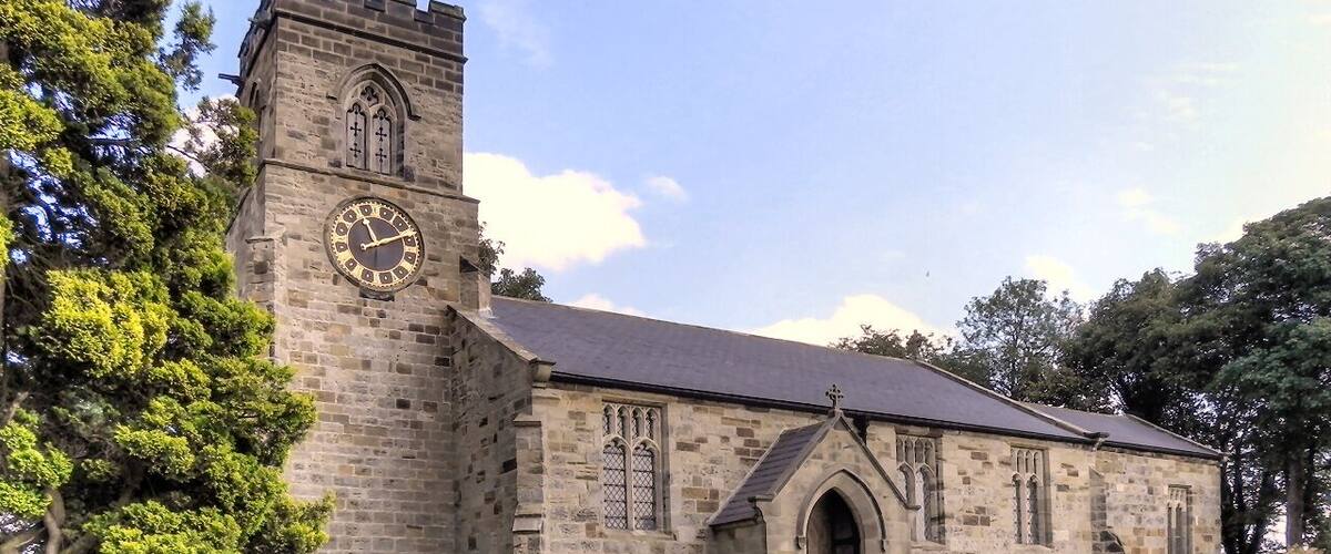 A stone church with a clock tower and a large tree in front.