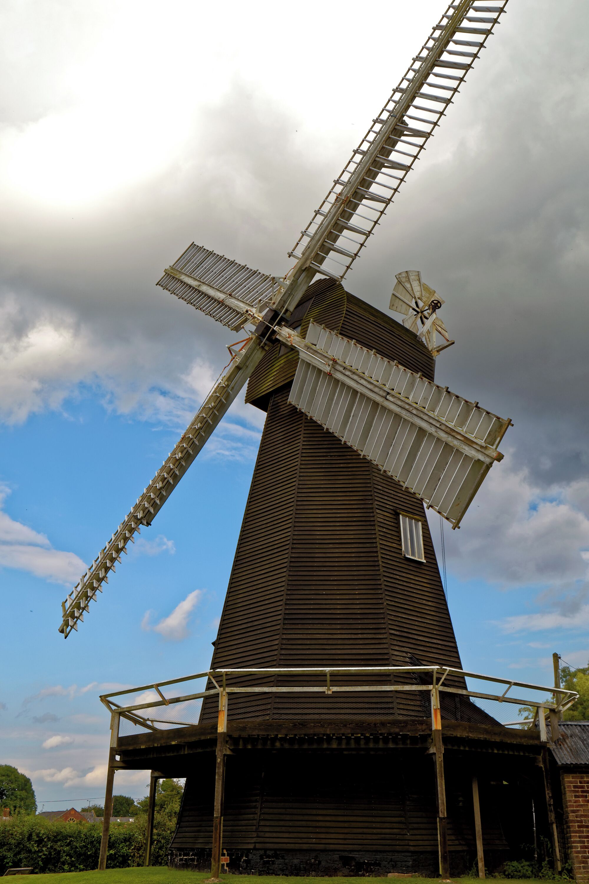 A large wooden windmill with a metal framework, set against a partly cloudy sky.