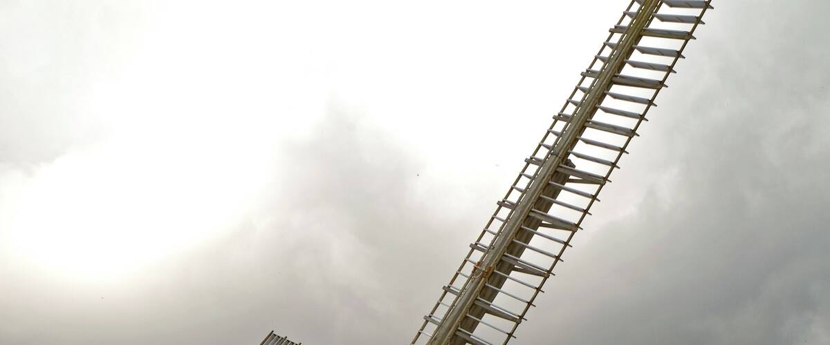 A large wooden windmill with a metal framework, set against a partly cloudy sky.