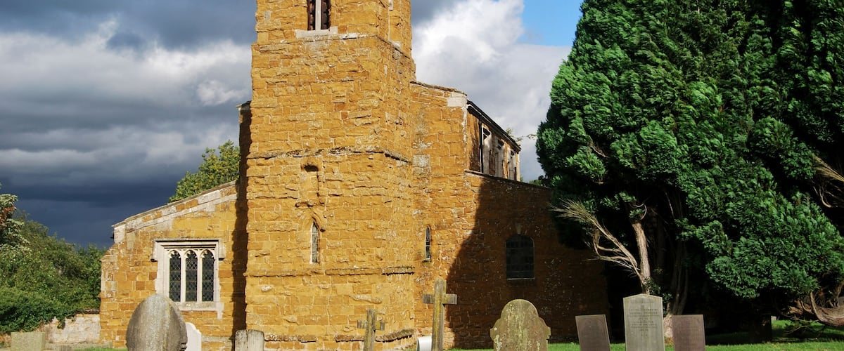 A historic stone church with a tall tower and a graveyard in front.