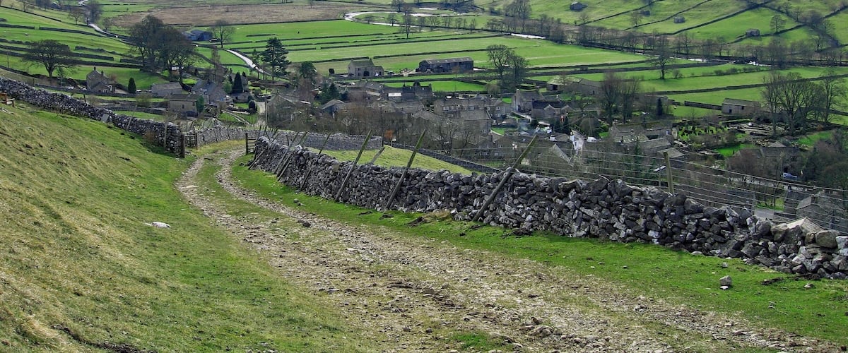 A rural landscape with rolling hills, stone walls, and scattered houses.