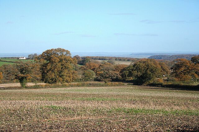 A rural landscape with fields, trees, and distant hills.