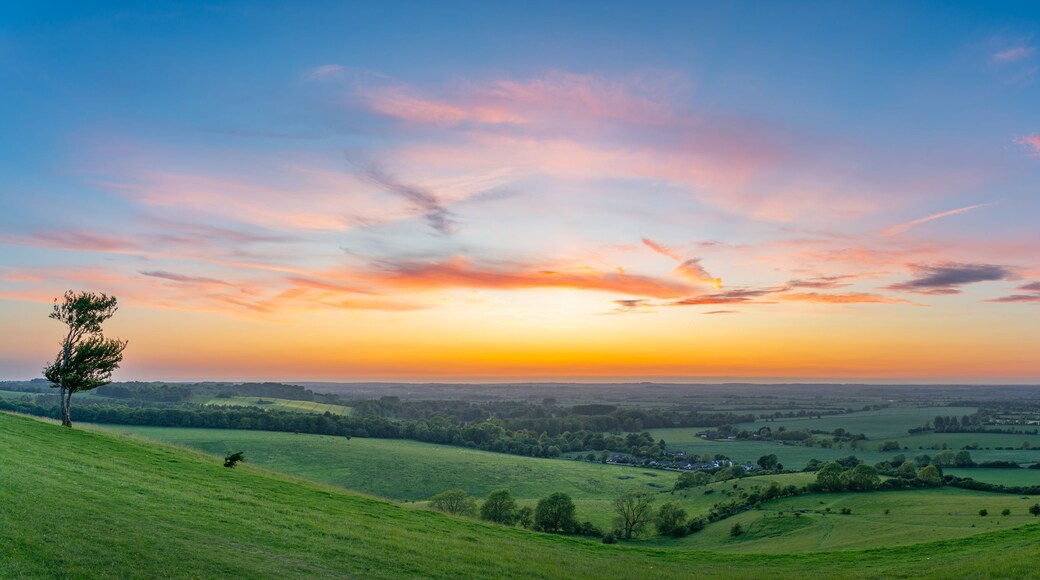 A panoramic view of a hilly landscape during sunset with a clear sky.
