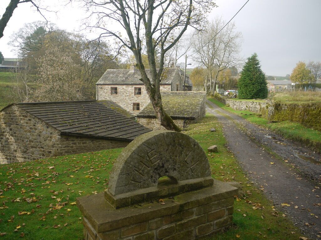 A stone house with a thatched roof, a stone wall, and a circular stone structure in the foreground.