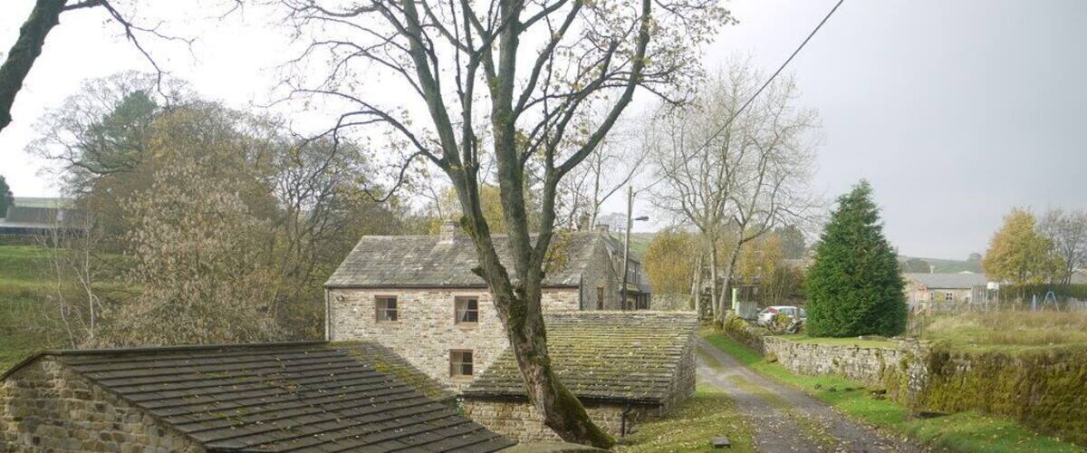 A stone house with a thatched roof, a stone wall, and a circular stone structure in the foreground.