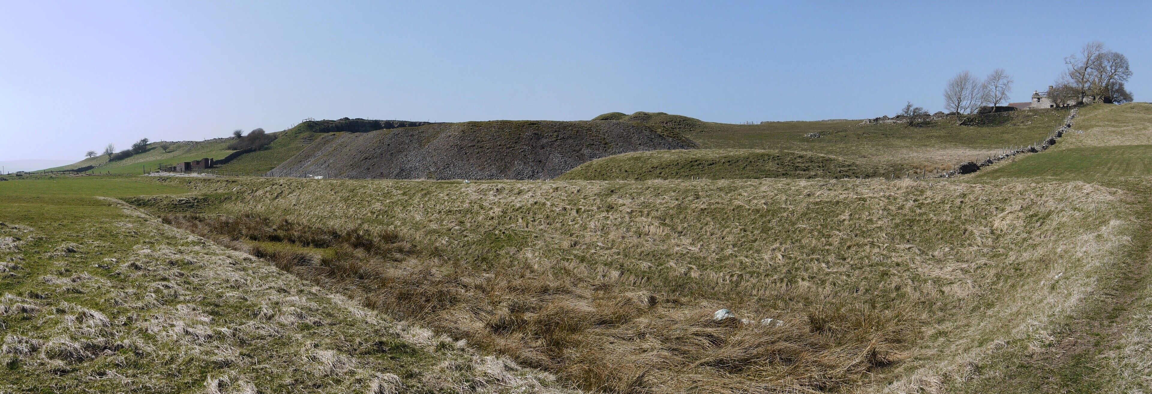 A grassy hillside with a ditch and a stone wall.