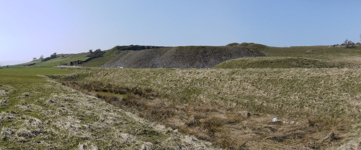 A grassy hillside with a ditch and a stone wall.