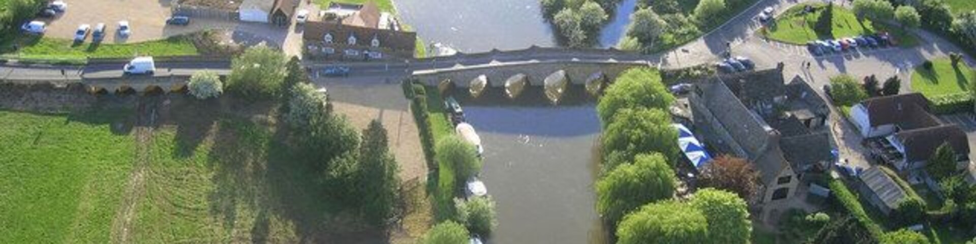 Vista aérea de un río con un puente, rodeado de campos verdes y árboles.