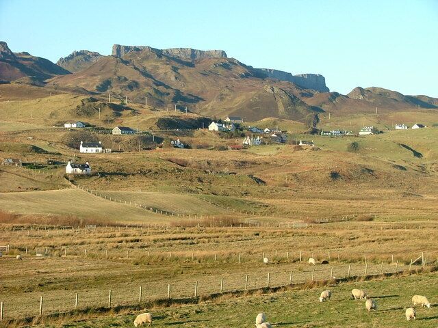 A rural landscape with rolling hills, scattered white houses, and grazing sheep.