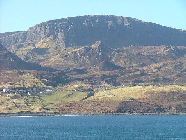 A coastal landscape with a prominent mountain, a small settlement, and a body of water.