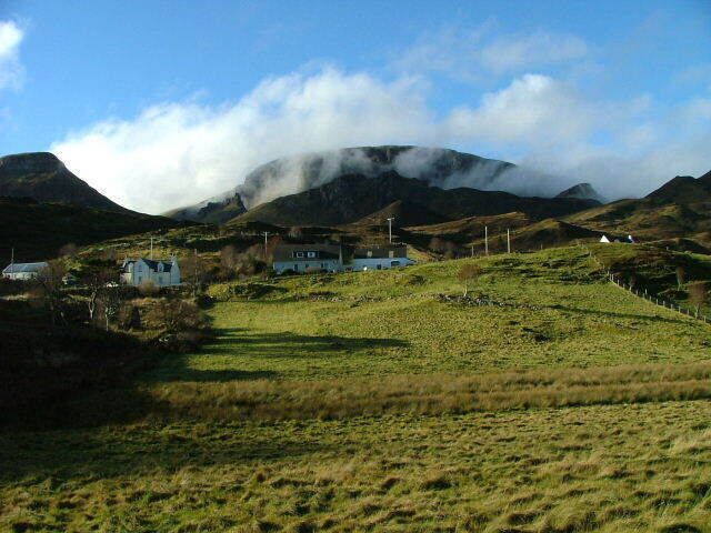 A rural landscape with rolling hills, a few houses, and a mountain partially obscured by clouds.
