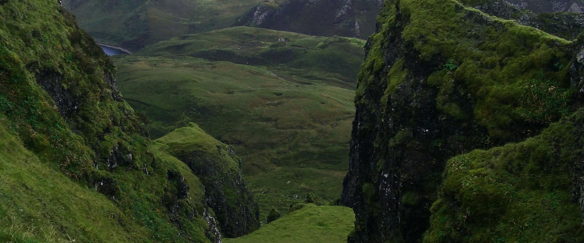 A mountainous landscape with green valleys and a body of water in the distance.