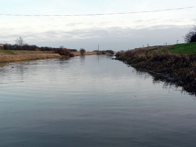 A calm river with grassy banks and a distant power line.