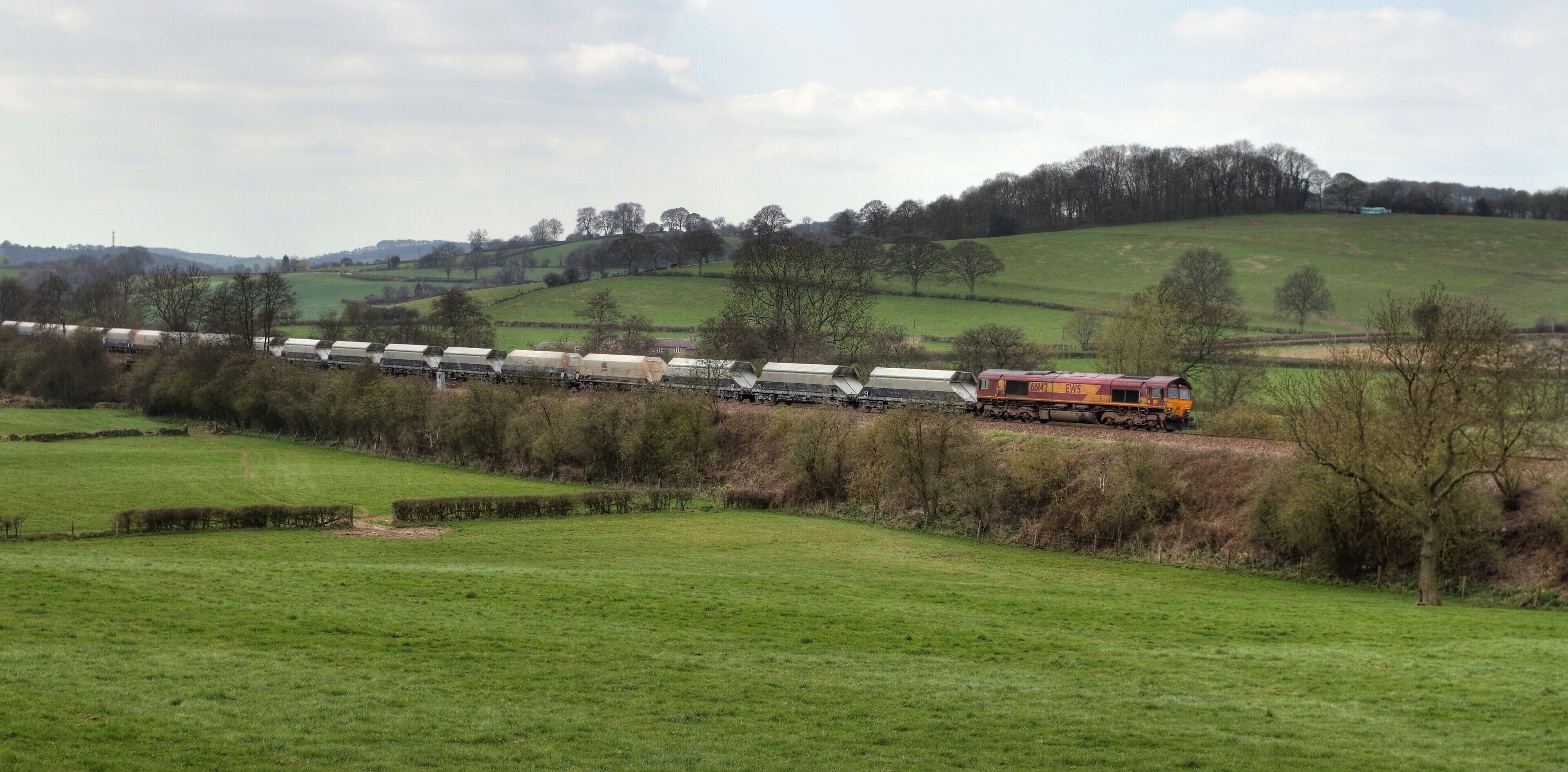 A train moving through a rural landscape with green fields and rolling hills.