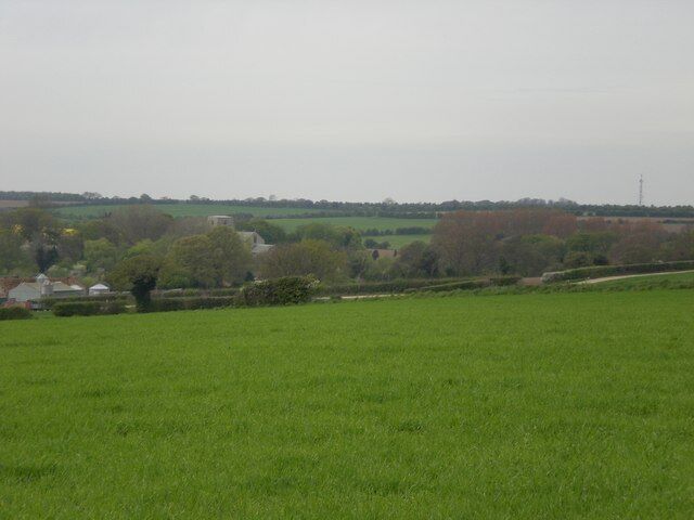 A green field with a rural landscape, houses, and trees in the distance.