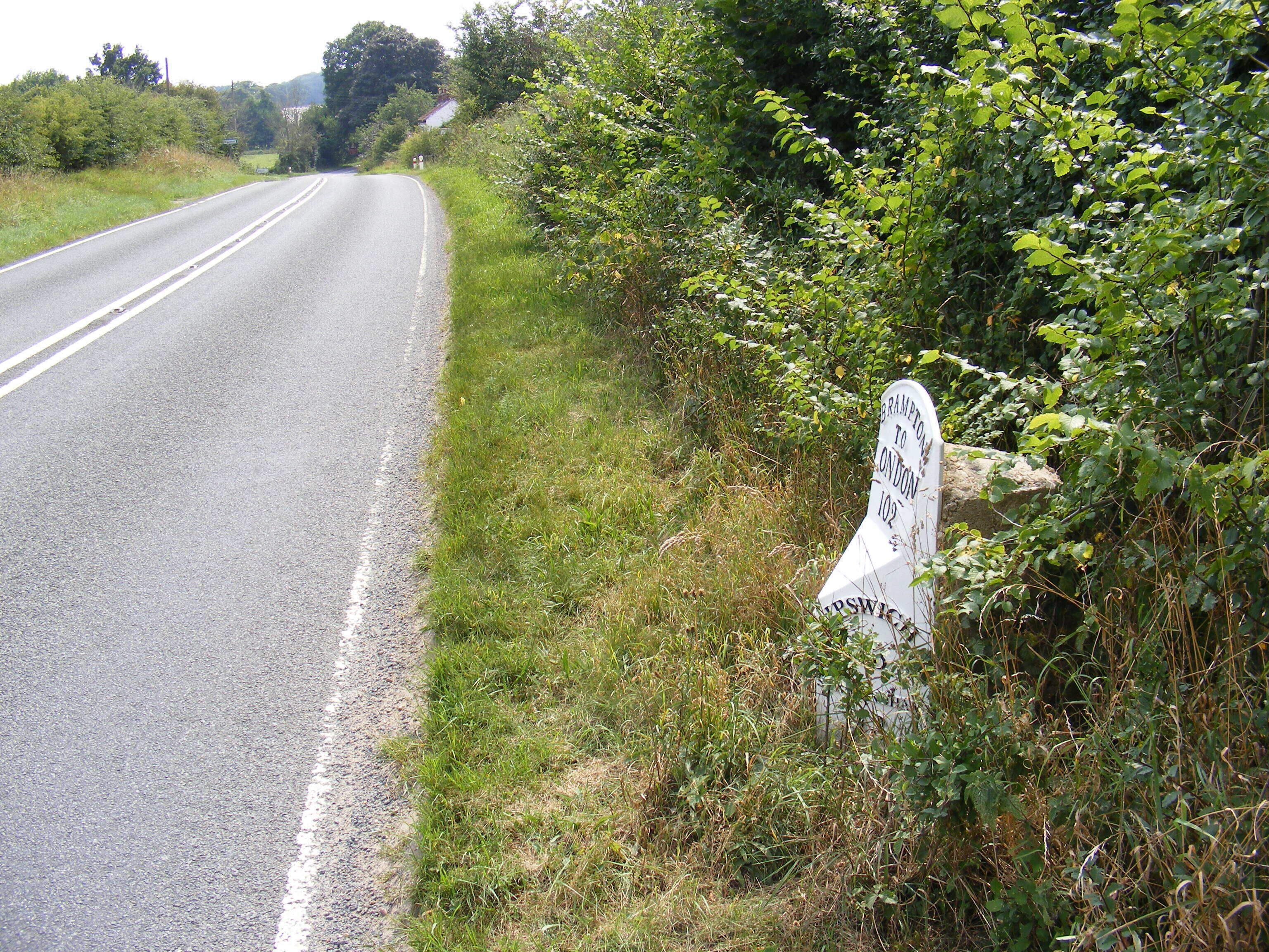A rural road with a white directional sign indicating 'Brampton to London via 102' and 'Windsor'.