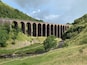 A stone viaduct over a river in a hilly area.