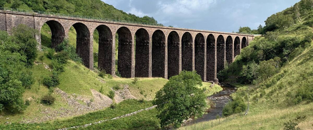 A stone viaduct over a river in a hilly area.