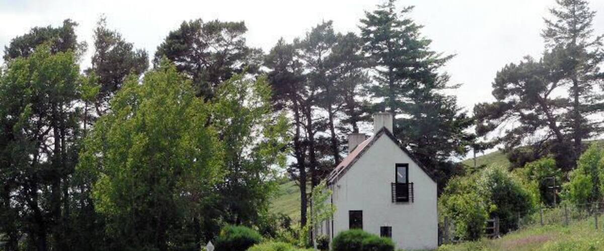 A white house with a red roof surrounded by trees and a winding road.