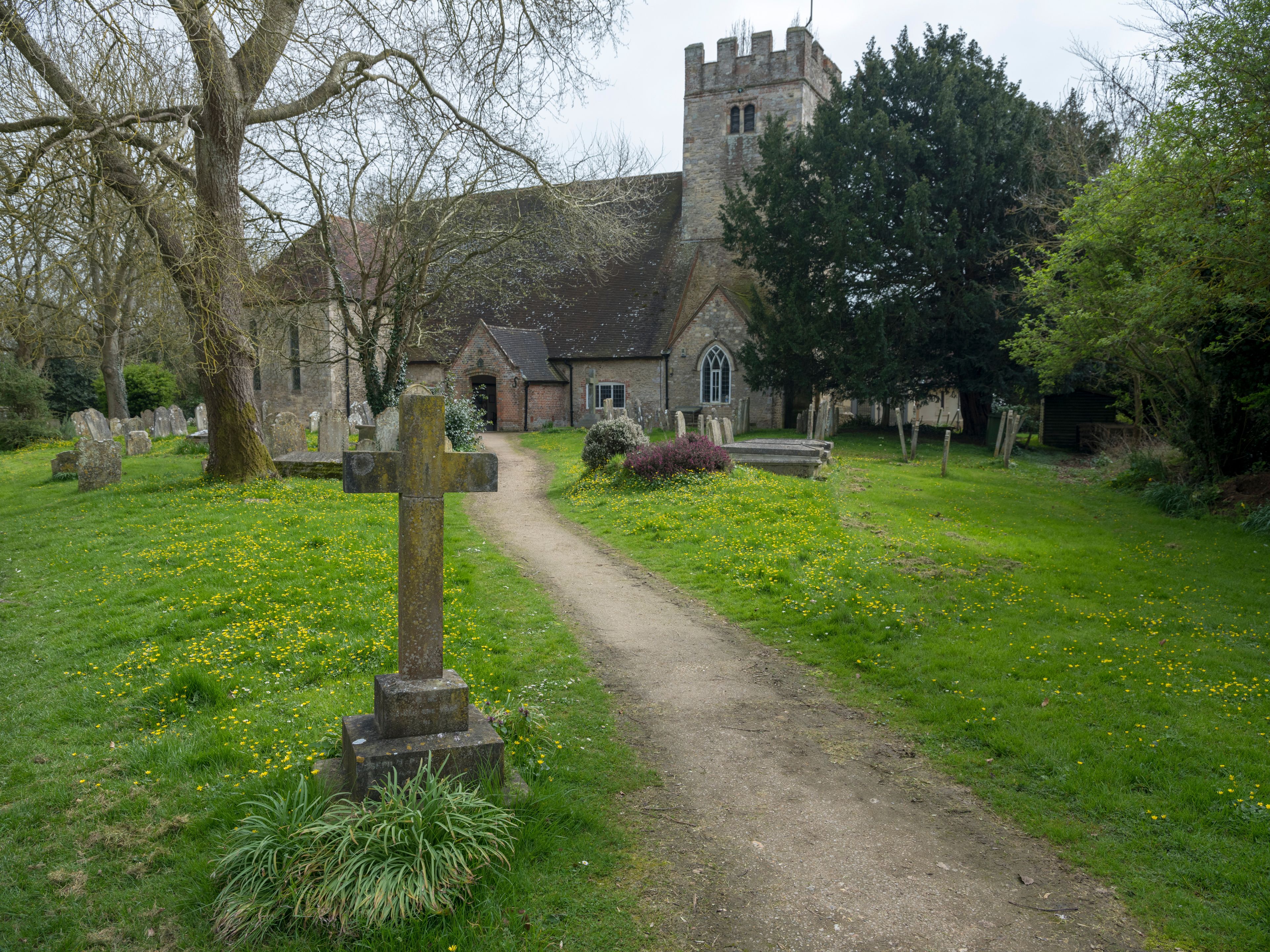 A church with a tower, surrounded by a cemetery with headstones and a cross in the foreground.