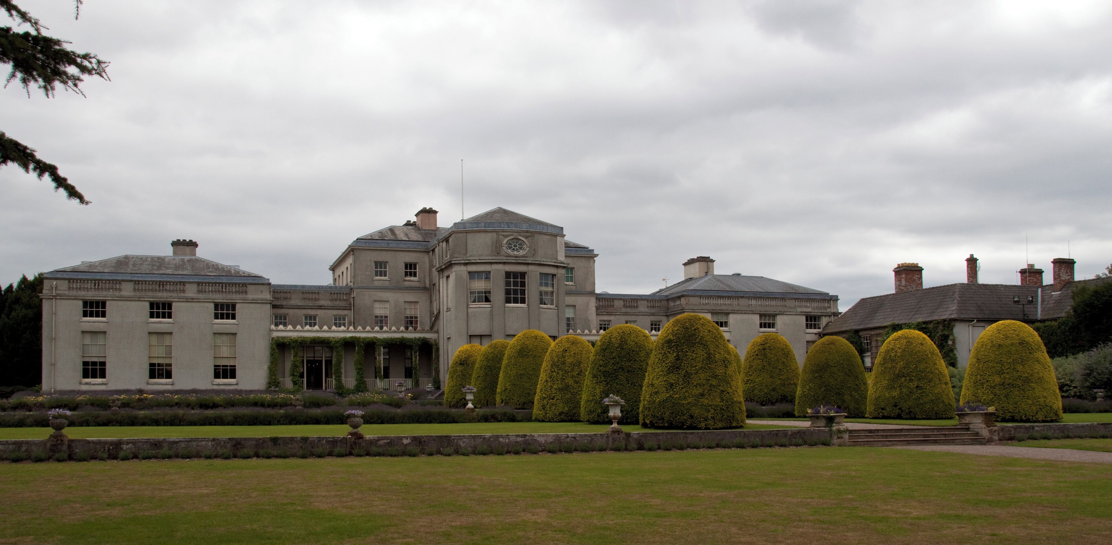 A large stately building with a symmetrical facade, a central dome, and a formal garden with neatly trimmed topiary.