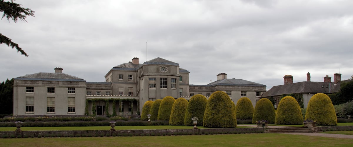 A large stately building with a symmetrical facade, a central dome, and a formal garden with neatly trimmed topiary.
