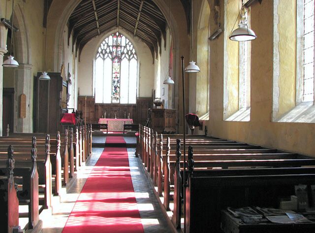 The church of SS Peter and Paul in Shropham - view east. St Peter's church > 1761300 is situated to the east of the village of Shropham, adjoined by the former vicarage. It has a massive tower which dates from the 16th century but the church building is much older. However, much of the soft stone used in building it has deteriorated and had to be replaced over the centuries. The fine north doorway > 1761345 dates from the 13th century as does the arcade inside. Apart from minor repairs, the arch-braced timber roof in the nave is original. Font > 1761448 and cover are Jacobean. The church was restored in Victorian times and most furnishings date from that time. There is one medieval carved bench end which depicts a dog > 1761417 - it marks the family pew of the Barkers, Lords of Shropham Manor, which was built for the Barker family in the 1720s. The carved reredos > 1761393 is modern and commemorates Augustus Hethersett Hemsworth who died in WW1. The stained glass in the east window > 1761389 is Victorian.