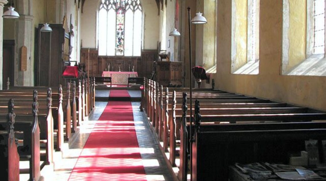 The church of SS Peter and Paul in Shropham - view east. St Peter's church > 1761300 is situated to the east of the village of Shropham, adjoined by the former vicarage. It has a massive tower which dates from the 16th century but the church building is much older. However, much of the soft stone used in building it has deteriorated and had to be replaced over the centuries. The fine north doorway > 1761345 dates from the 13th century as does the arcade inside. Apart from minor repairs, the arch-braced timber roof in the nave is original. Font > 1761448 and cover are Jacobean. The church was restored in Victorian times and most furnishings date from that time. There is one medieval carved bench end which depicts a dog > 1761417 - it marks the family pew of the Barkers, Lords of Shropham Manor, which was built for the Barker family in the 1720s. The carved reredos > 1761393 is modern and commemorates Augustus Hethersett Hemsworth who died in WW1. The stained glass in the east window > 1761389 is Victorian.